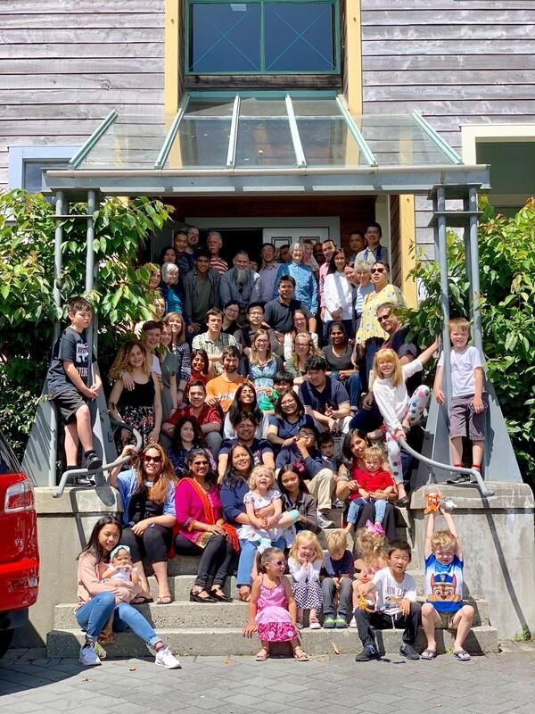 About fifty members of the church, all ages, smiling together on the front steps at Webb Street on a sunny day.